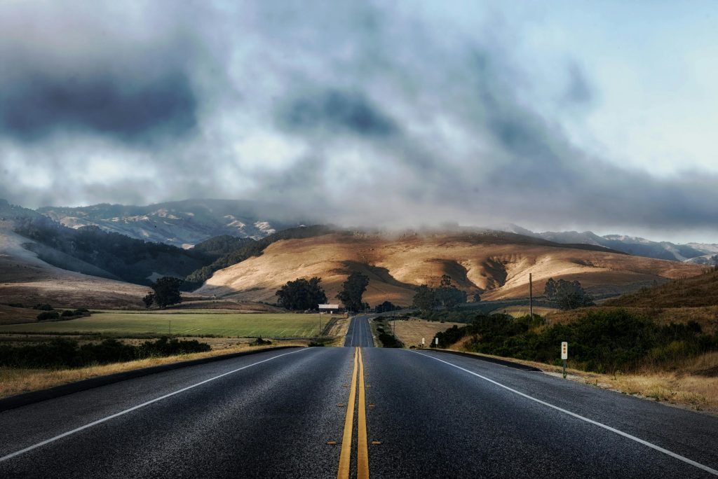 Dramatic sky over a deserted highway flanked by rolling hills, ideal for travel themes.